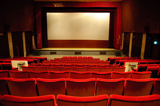 photograph shot from the back of an empty cinema, showing rows of bright red seats facing a blank screen
