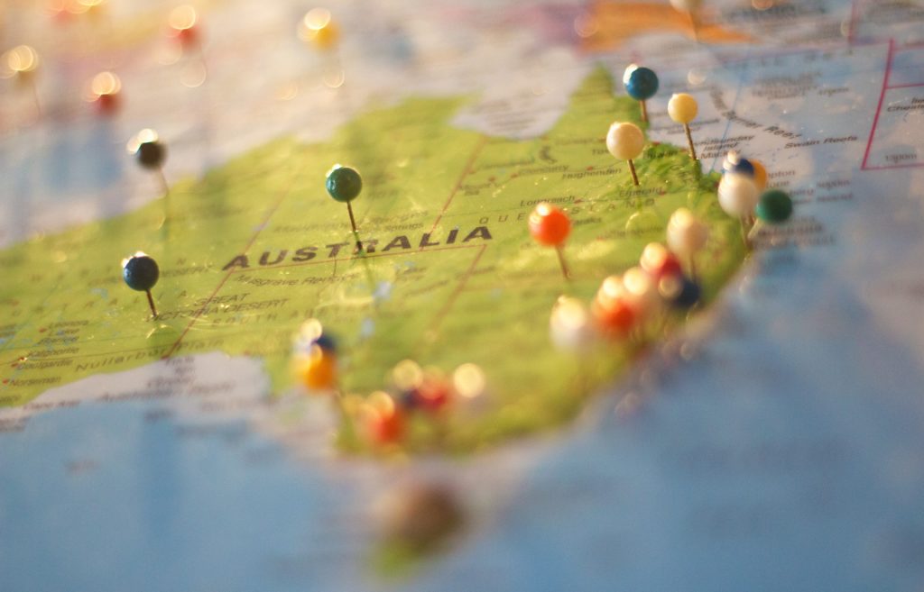 The image depicts a close up photograph of Australia on a map, with place names and state boundaries visible. Pins have been placed in various locations on the map, mainly down the East coast. 