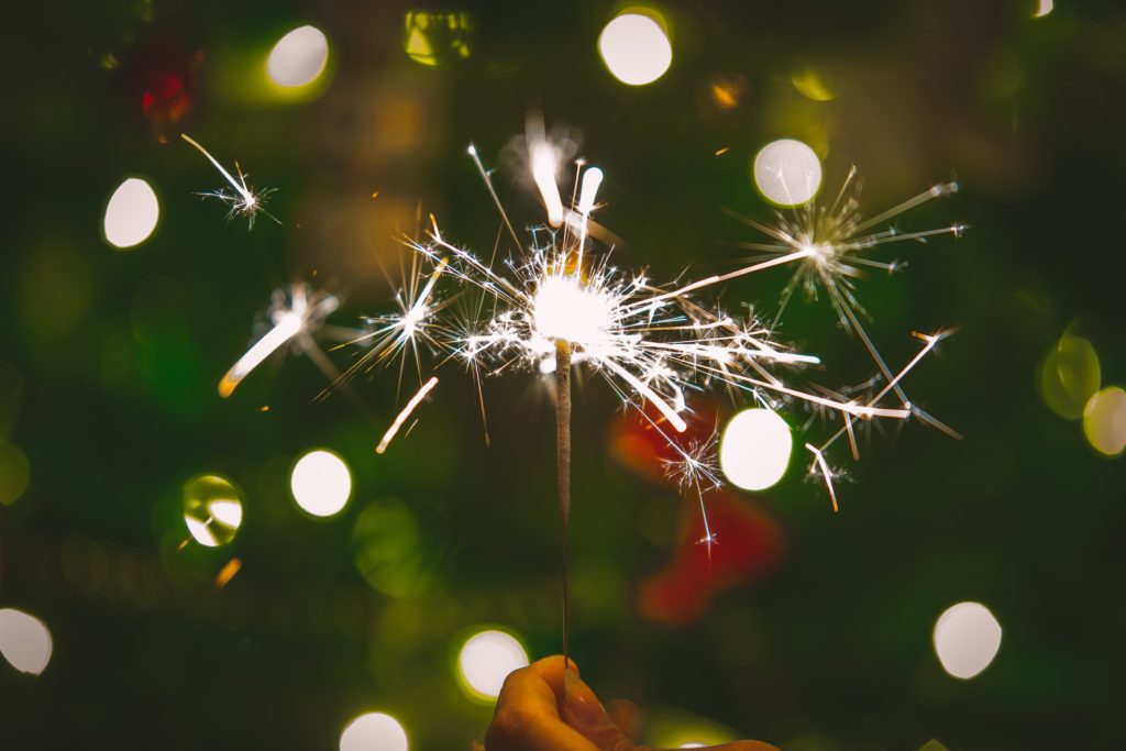 A close up image of a lit sparkler against a festive green background