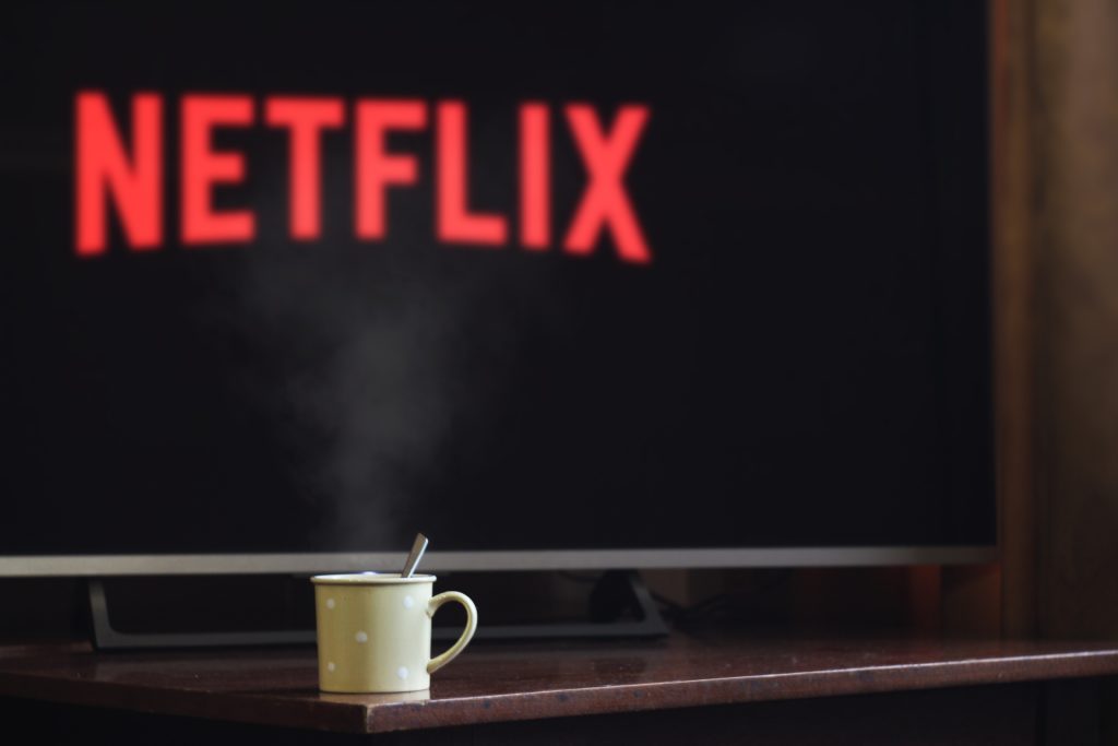 Photograph of a coffee mug sitting in front of a flat screen television showing the Netflix logo