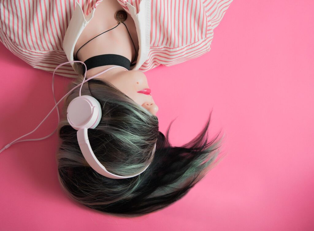 Photograph of a girl wearing pink lipstick, lying on the floor listening to headphones. Her dark hair swirles around her head, covering her eyes and the top of her head..